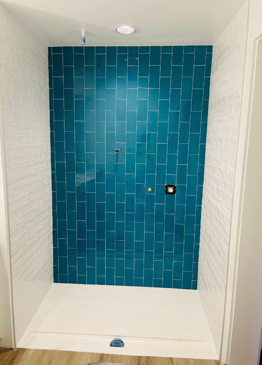Bathroom shower with a teal tile accent wall and white side walls