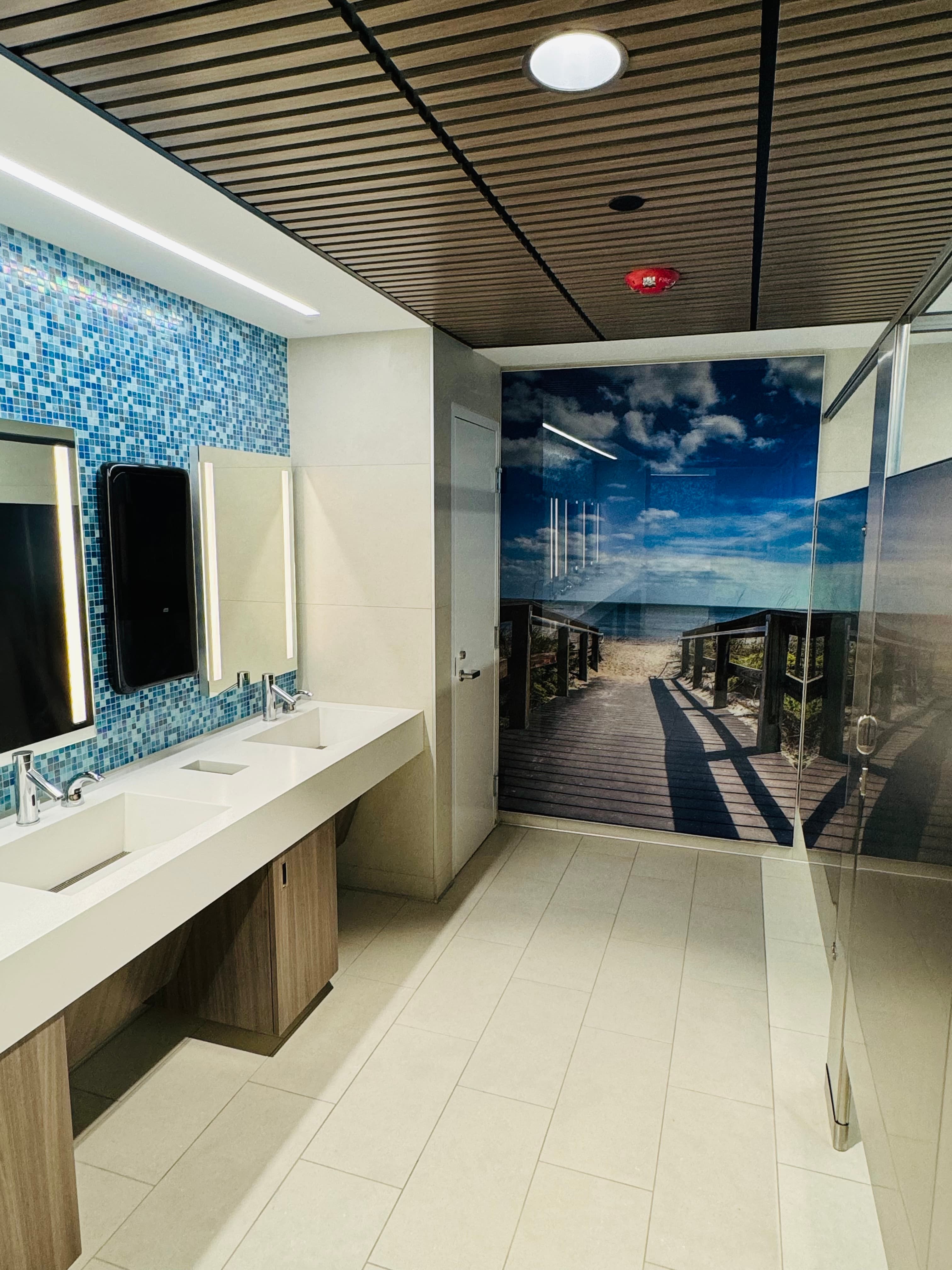 Commercial bathroom with double sinks, blue mosaic tile, and a beach mural