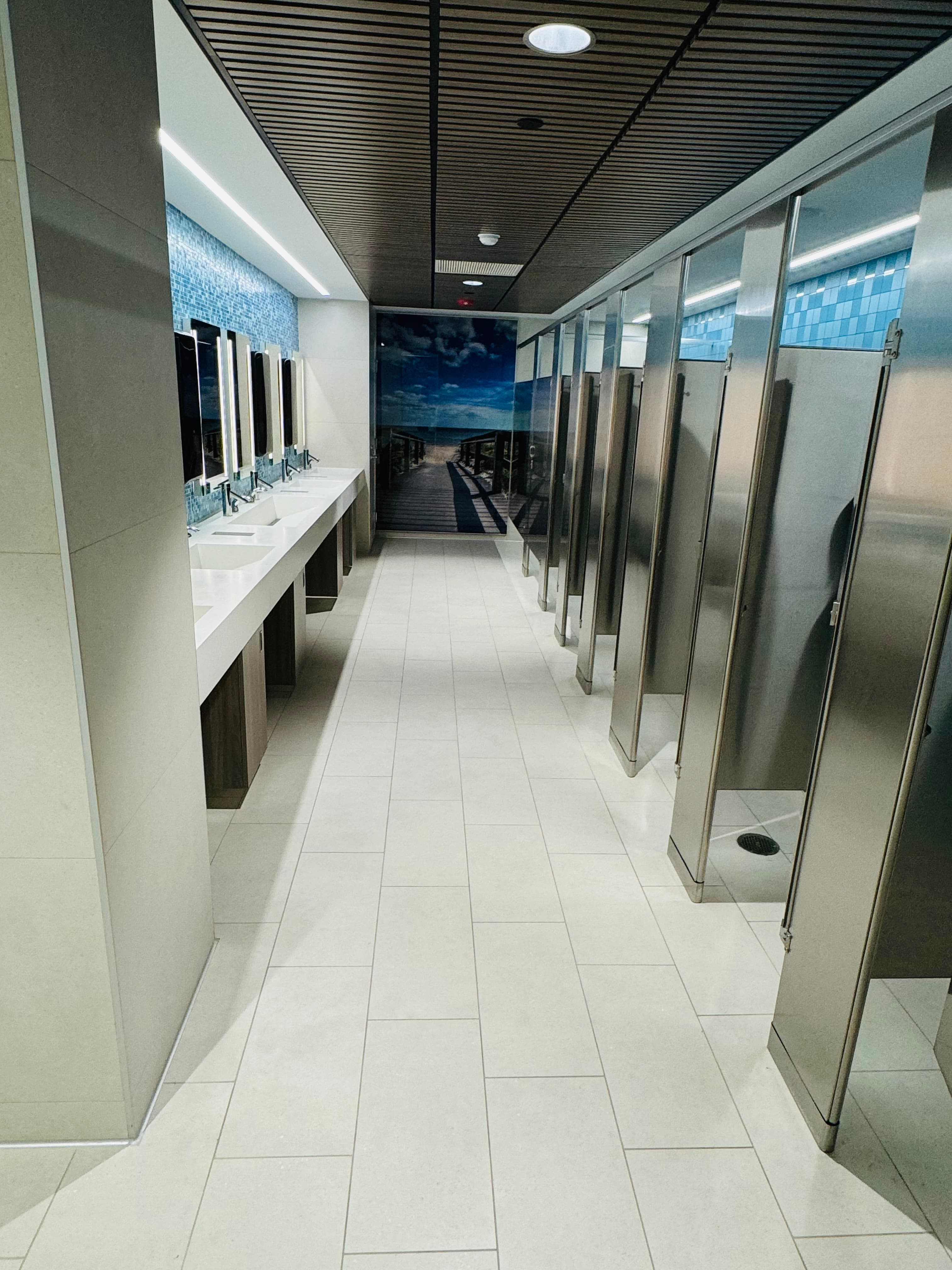 Commercial bathroom with tiled floor, blue mosaic backsplash, and metal stalls
