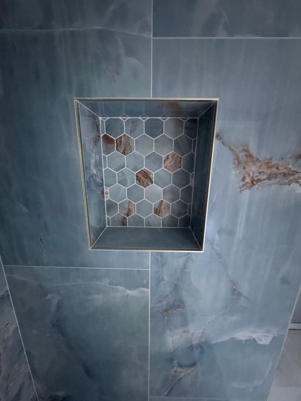 Bathroom shower niche with blue marble-look tile and hexagon mosaic detail
