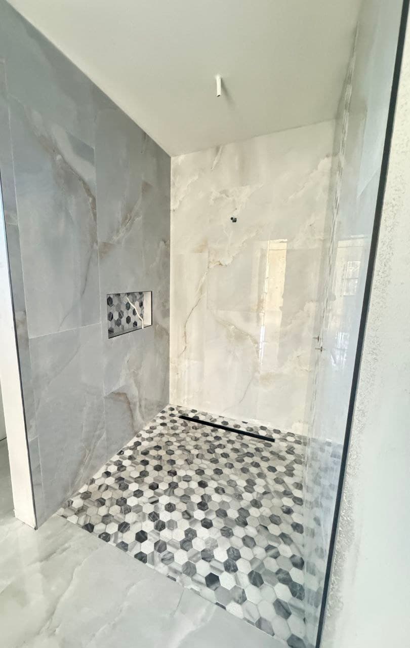 Bathroom walk-in shower with marble-look wall tile and a hexagon mosaic floor